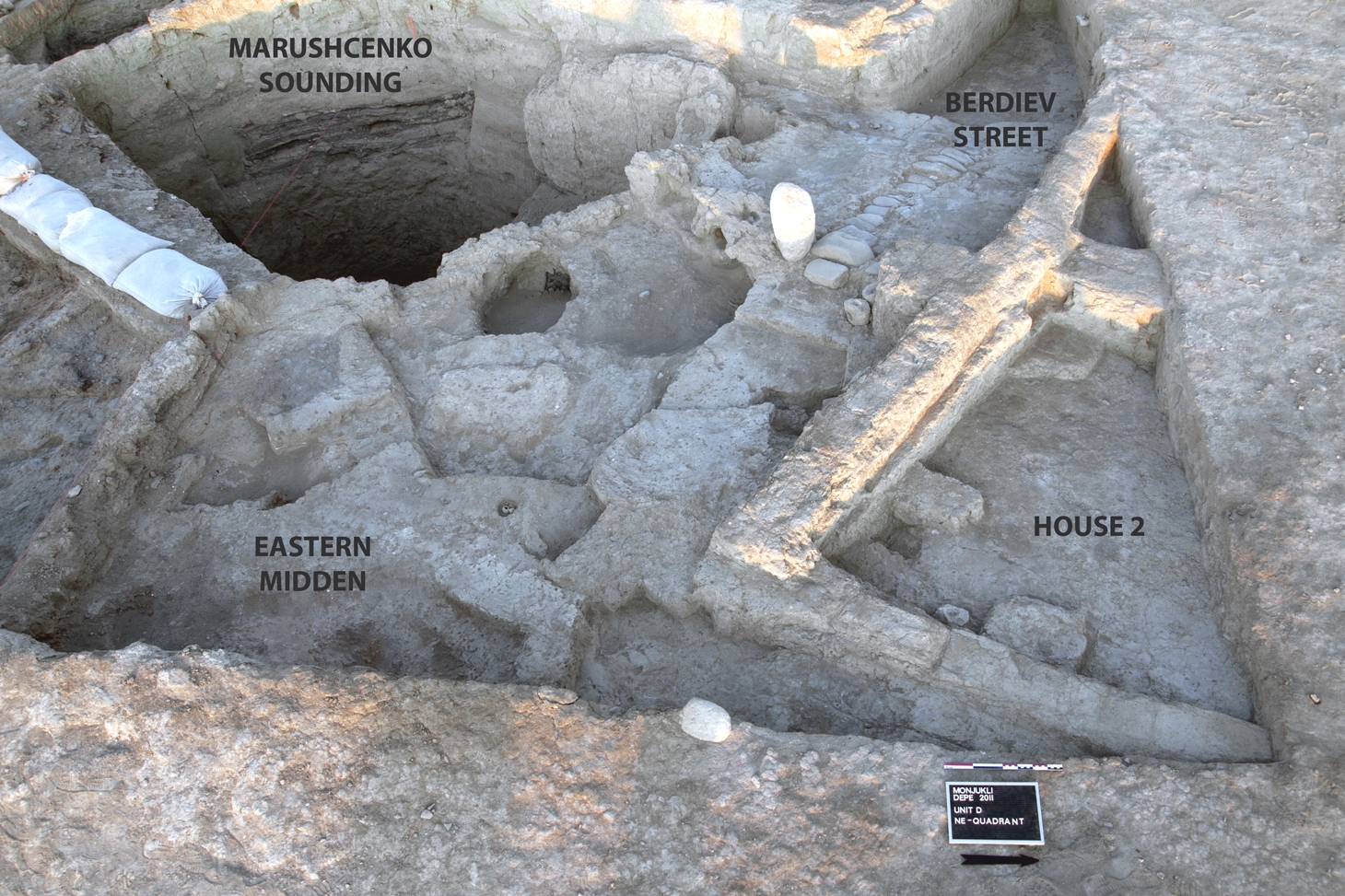Juxtaposition of architecture and features in Unit D at the close of the 2011 excavation season. The paved section of Berdiev Street ended at Gate 1, marked by a large standing limestone boulder. On the opposite side of the gate is the Eastern Midden. House 2 borders directly on Berdiev Street to the north. The sounding excavated by A. Marushchenko in 1959 cut into the midden as well as into architecture to the south (left side of the photo).