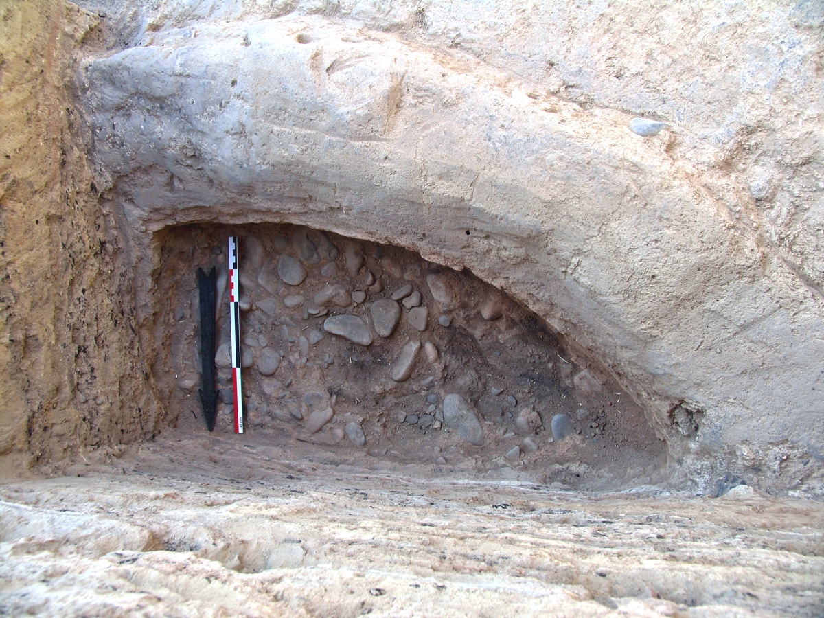 A portion of a large circular hearth, FI 5, outside Houses 7 and 8. The dense pebble layer visible here lay underneath a red burnt clay floor.