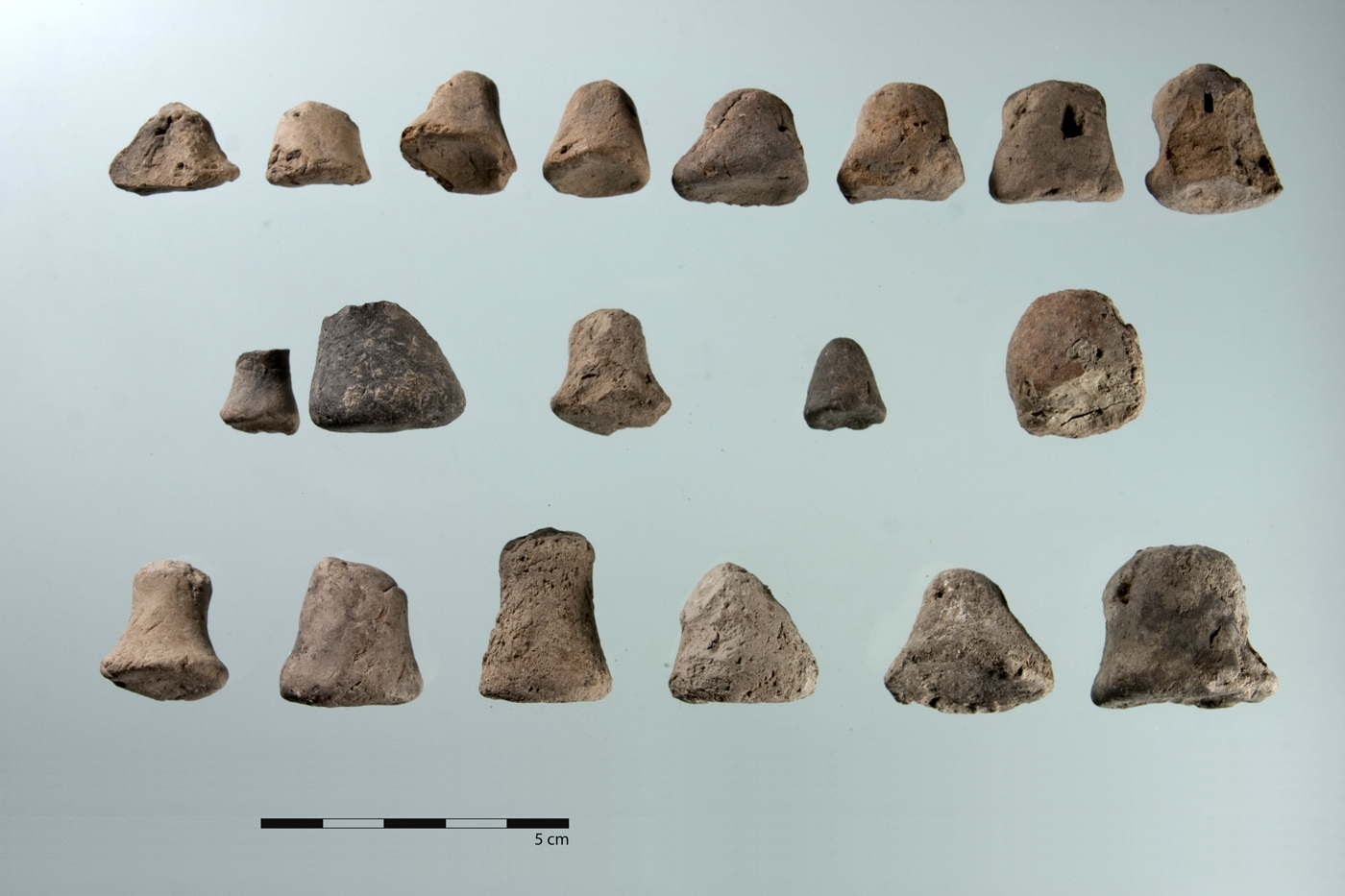 Squat, conical and pyramidal tokens. Several show punctures (for example, the two rightmost pieces in the upper row).